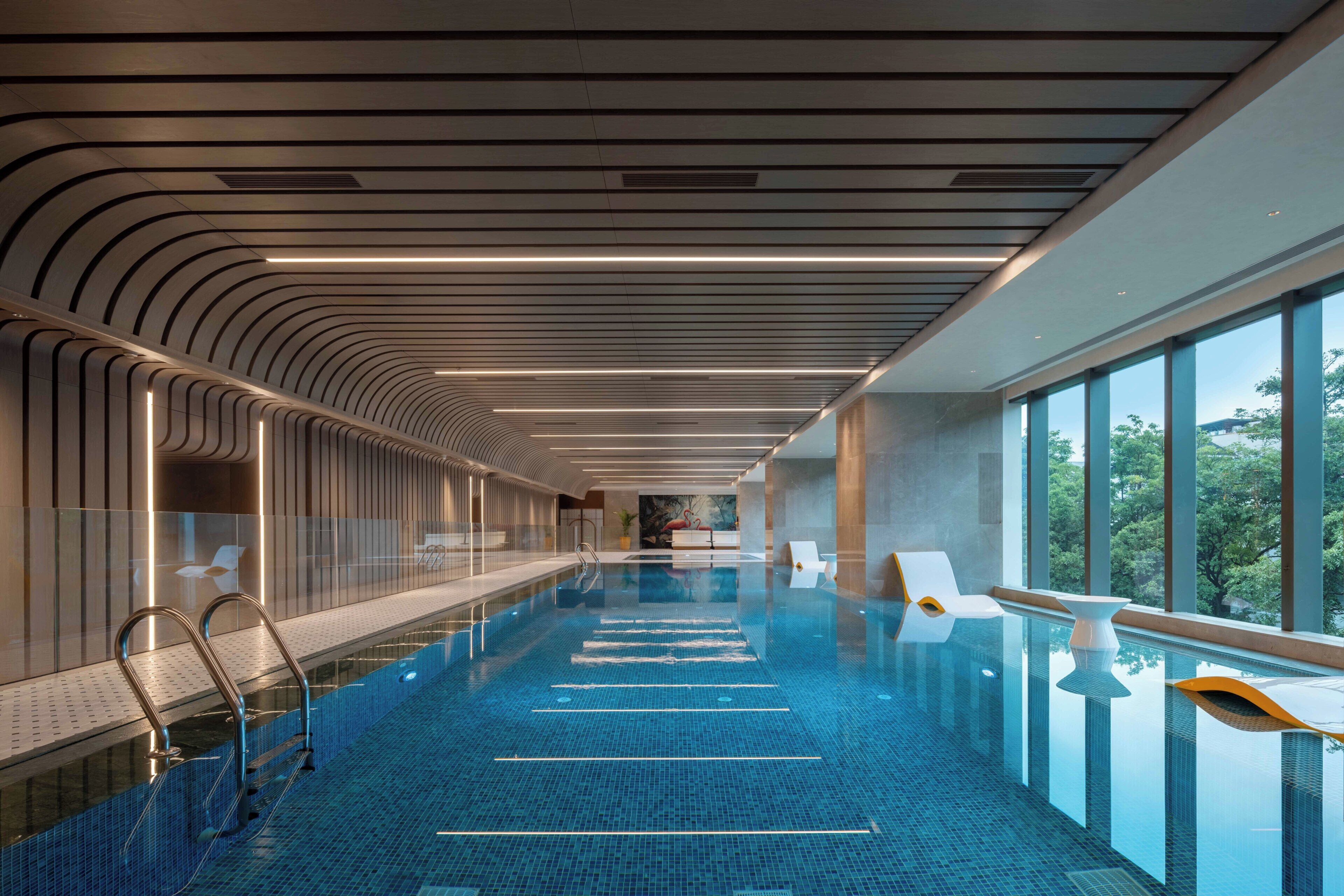 Piscina interior moderna com vista aberta para o exterior, área extensa à beira da piscina e design de teto marcante.