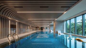 Piscina interior moderna com vista aberta para o exterior, área extensa à beira da piscina e design de teto marcante.