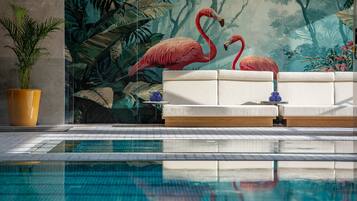 Zona de piscina con un sofá, una planta en maceta y un mural de flamencos.