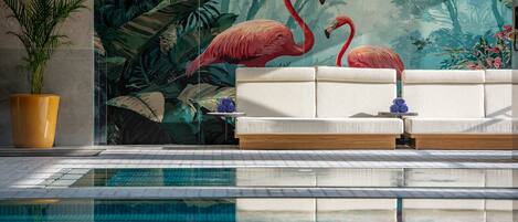 Zona de piscina con un sofá, una planta en maceta y un mural de flamencos.