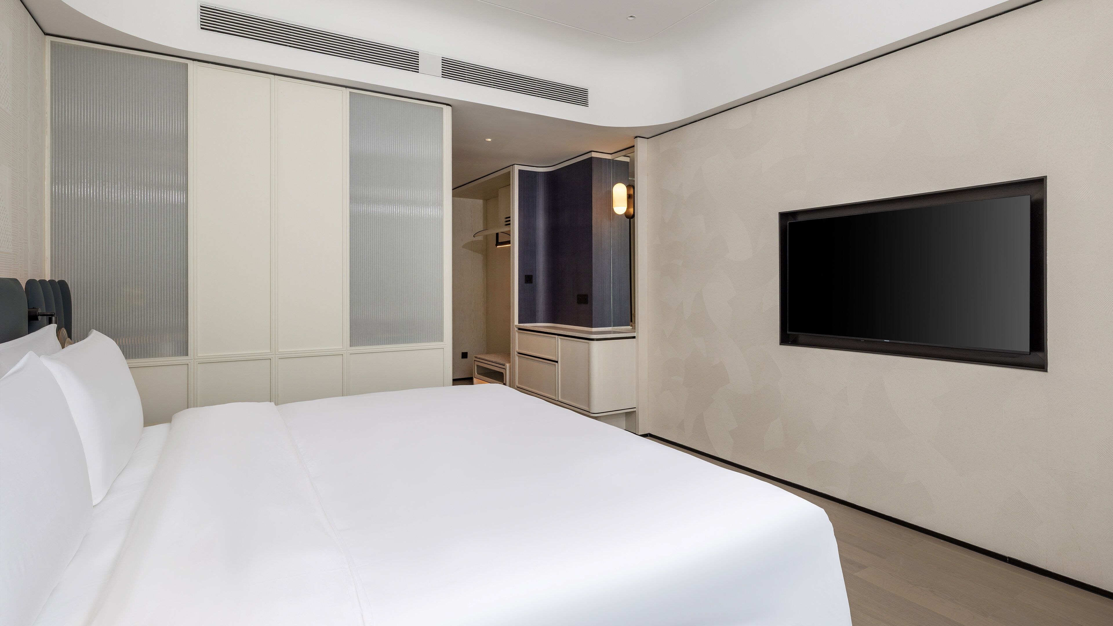Una habitación de hotel moderna con una cama grande, un televisor de pantalla plana en la pared y un vestidor.