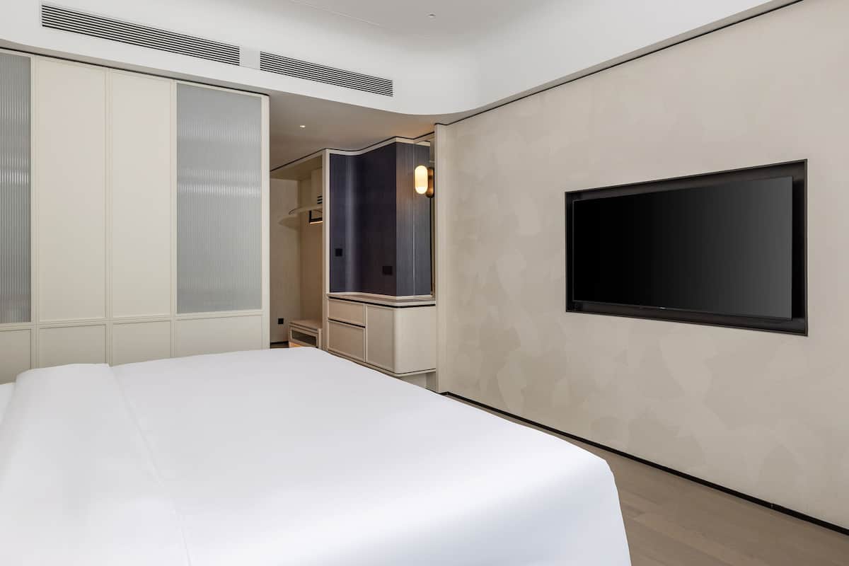 A modern hotel room with a large bed, a flat-screen TV mounted on the wall, and a walk-in closet.