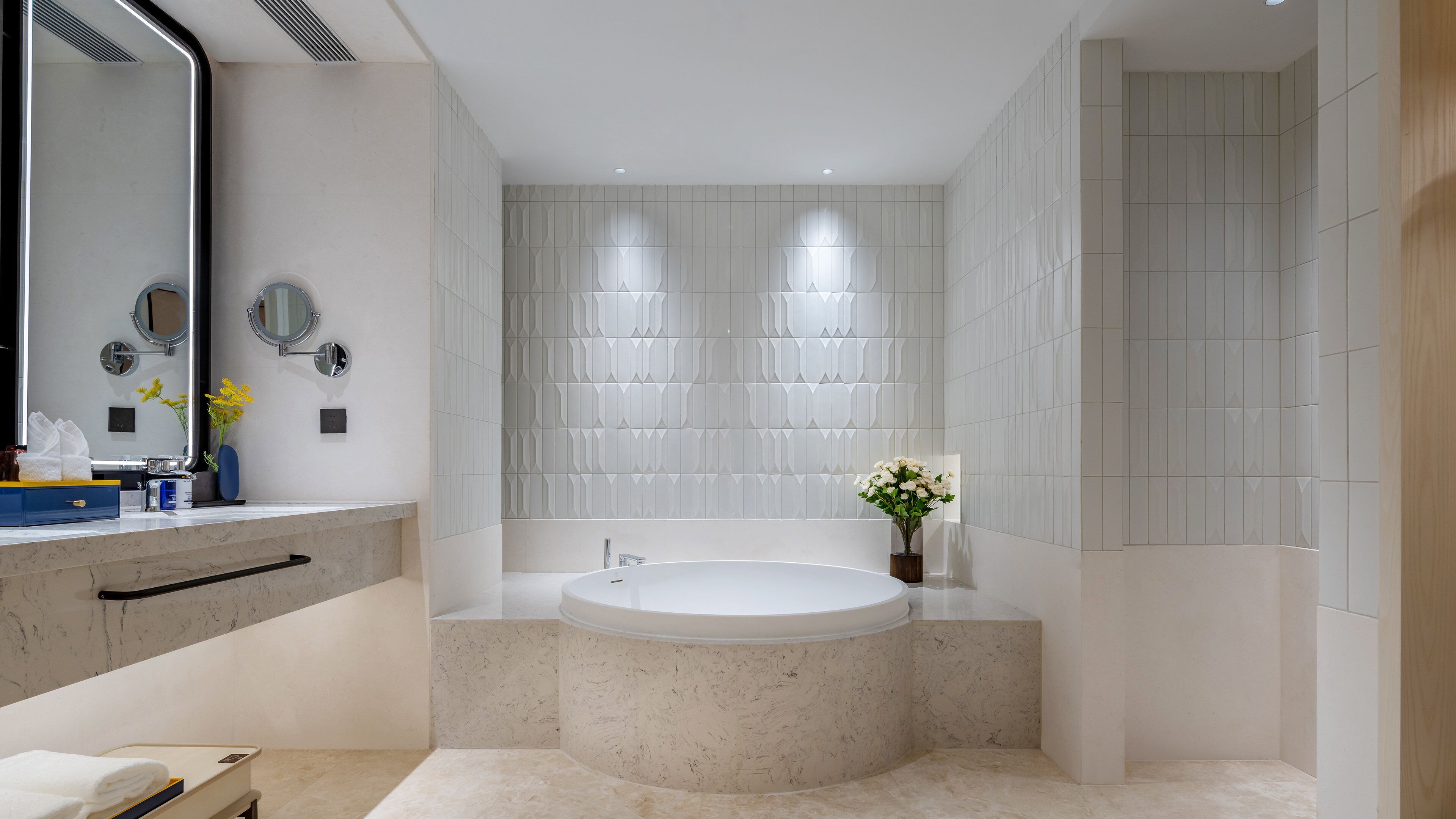 Un baño moderno con lavamanos de mármol, un espejo grande, una bañera independiente y un mueble de tocador empotrado.