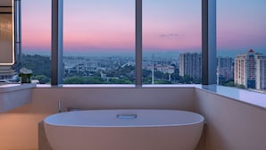 A modern bathroom with a large bathtub, a vase with flowers, and a cityscape view through large windows. - Xiamen Sm City By Ihg (Xiamen)