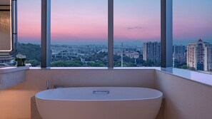 Un baño moderno con una bañera grande, un florero con flores y vistas a la ciudad a través de ventanales amplios.