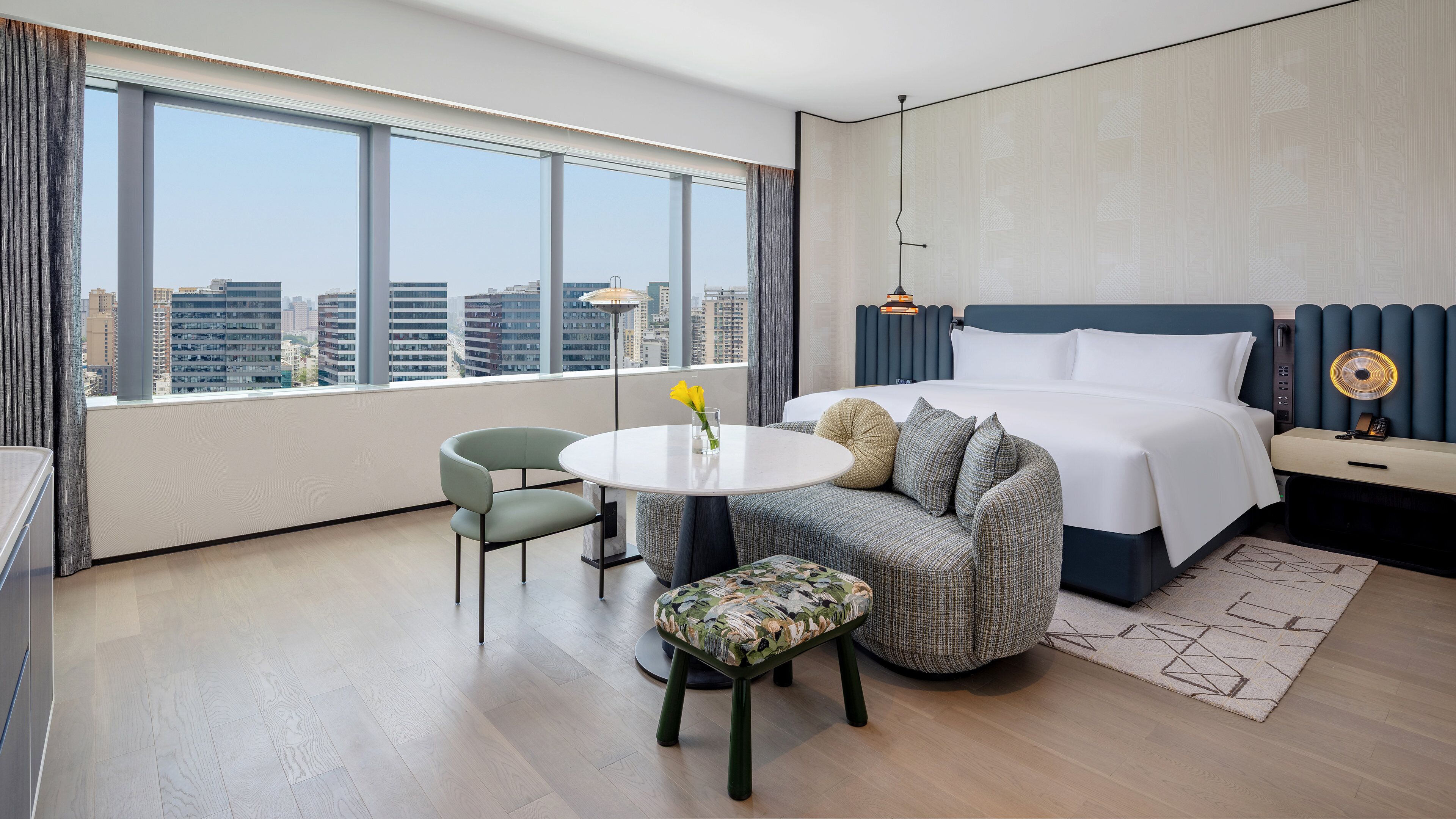 Una habitación de hotel moderna con un ventanal grande, una mesa redonda, un sofá y una cama.