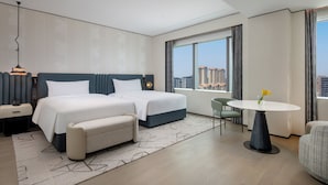 A hotel room with two beds, a small table with a vase, a chair, a nightstand with a phone, and a view of buildings. - Xiamen Sm City By Ihg (Xiamen)