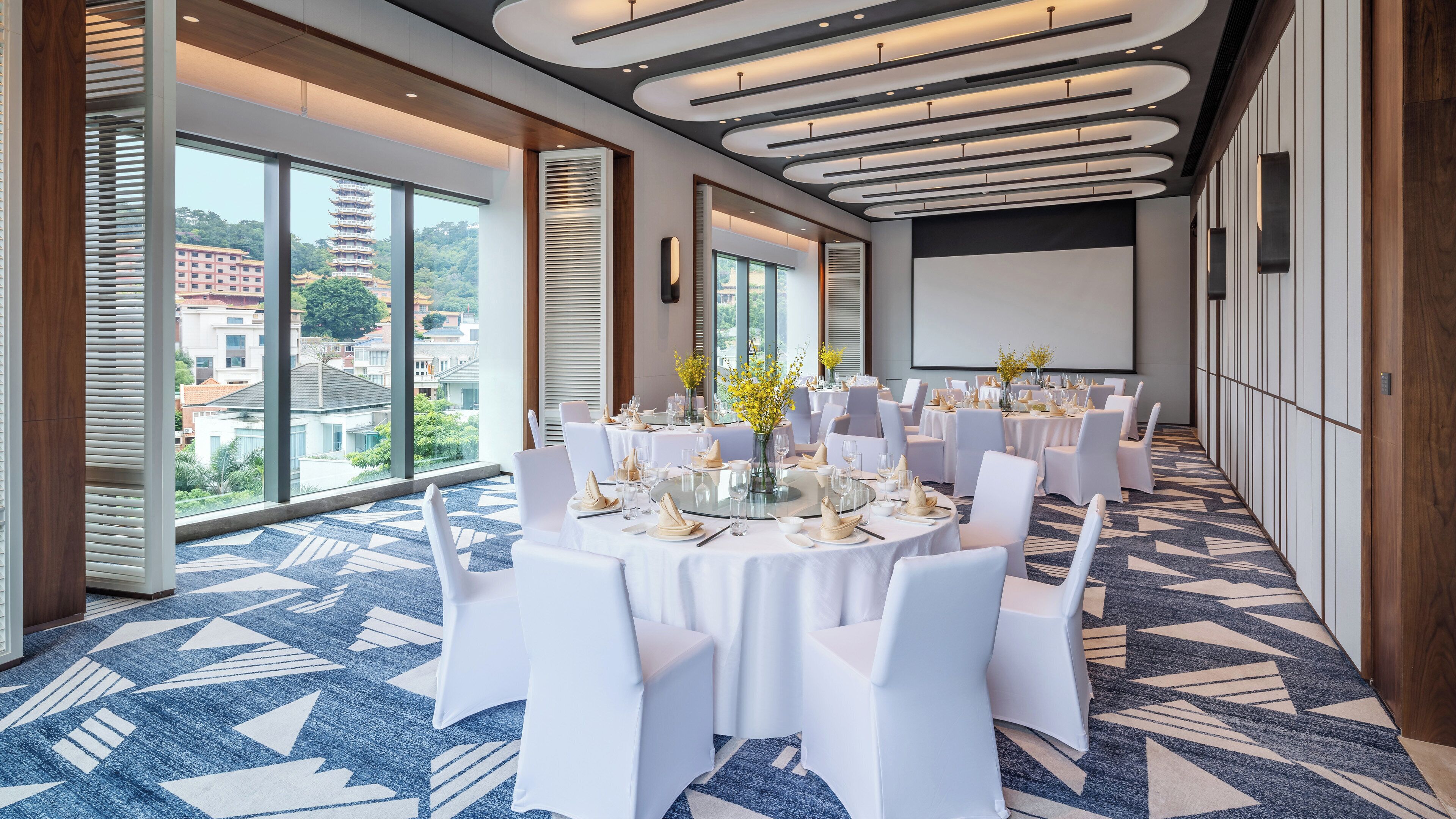 A conference room with round tables, white chairs, and a large screen.
