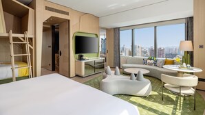 Ett hotellrum med en säng, ett skrivbord med en tv, en soffa, ett litet bord och utsikt över stadsbilden.