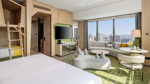 Habitación de hotel con cama, escritorio con televisor, sofá, una mesita y vista a la ciudad.
