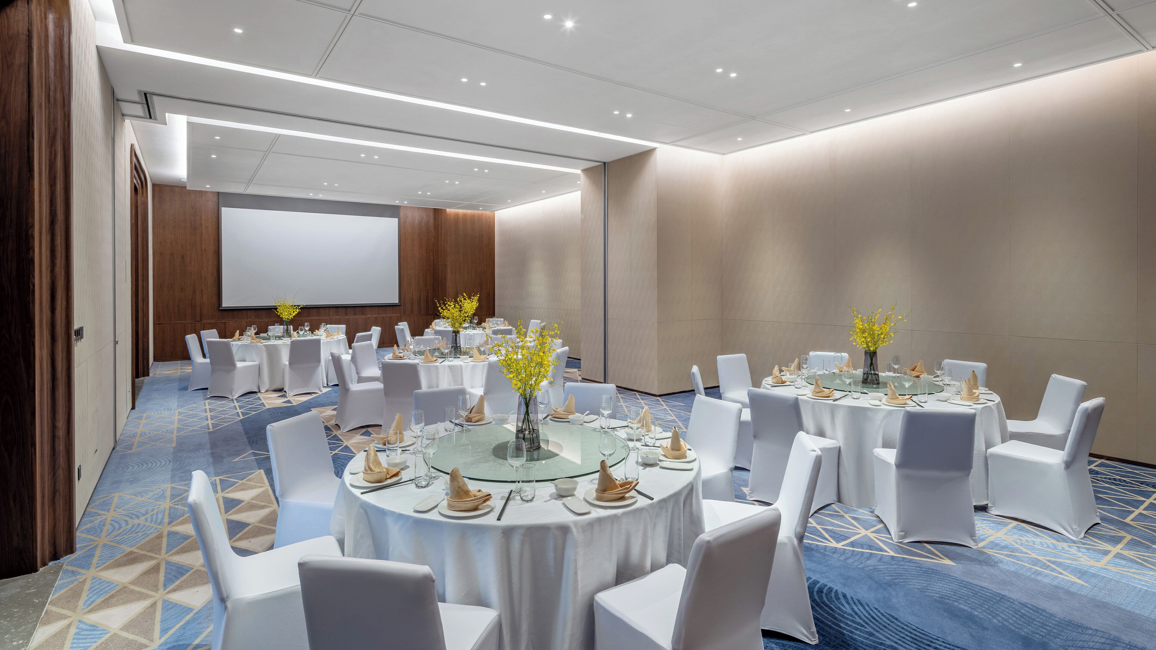 A conference room with round tables, white chairs, and a large screen.