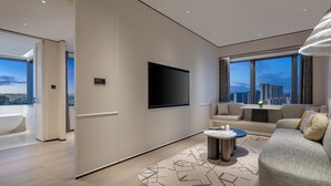 A modern living room with a flat-screen TV, a sofa, a coffee table, and a view of the cityscape. - Xiamen Sm City By Ihg (Xiamen)