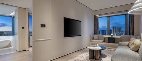 A modern living room with a flat-screen TV, a sofa, a coffee table, and a view of the cityscape.