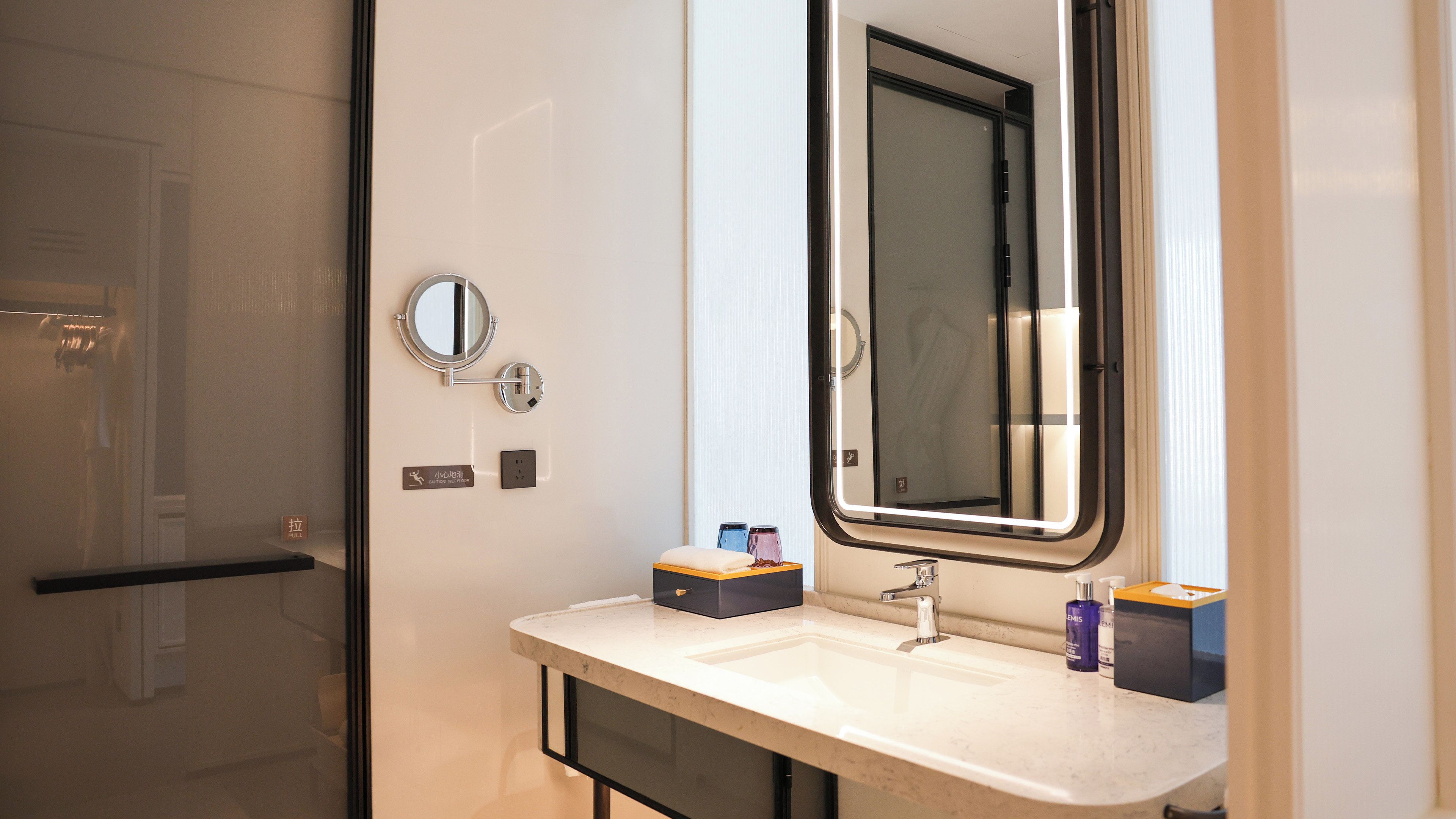 Une salle de bain moderne avec une douche à parois de verre, un lavabo avec un miroir et des articles de toilette posés sur le comptoir.