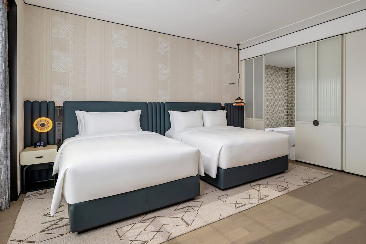 A modern hotel room with a bed, bedside tables, a nightstand, a mirror, and a wardrobe.