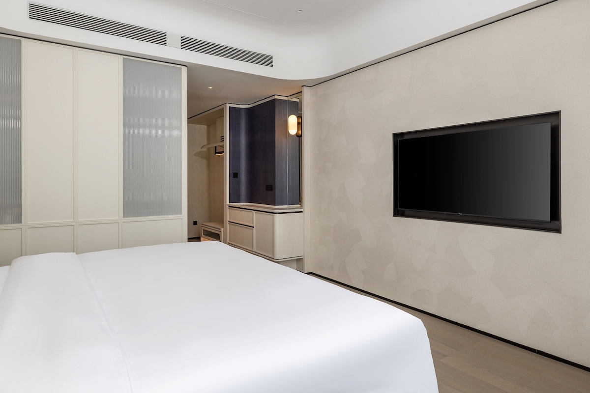 A modern hotel room with a large bed, a flat-screen TV mounted on the wall, and a walk-in closet.
