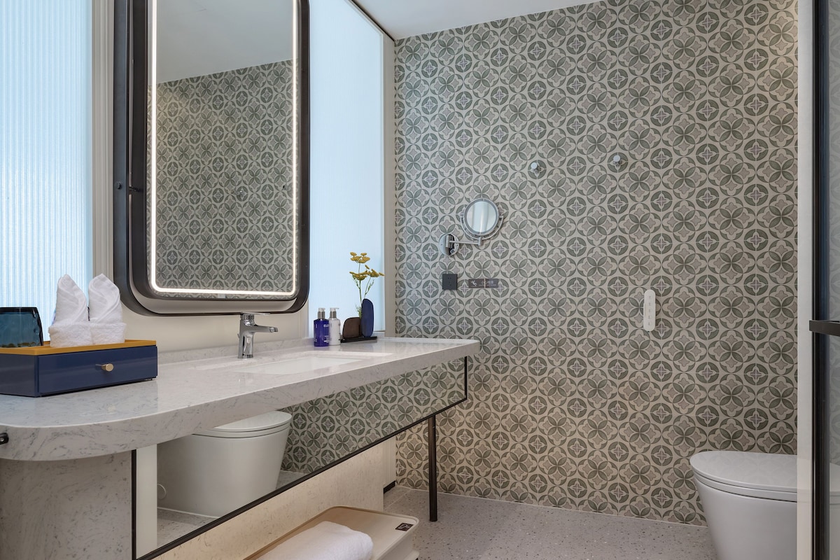 A bathroom with a marble sink, a mirror, a toilet, and patterned wallpaper.