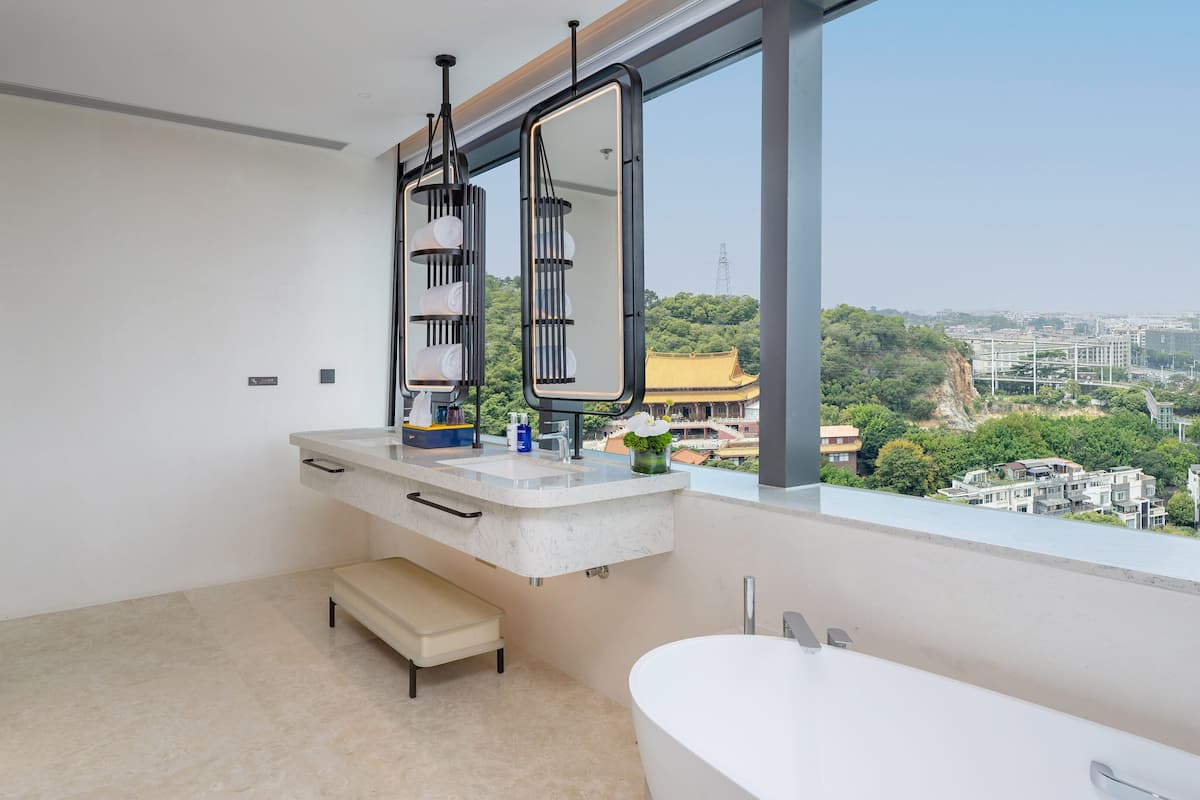 A modern bathroom with a bathtub, a vanity with a mirror, and a view of a cityscape through large windows.