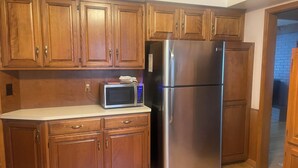 A kitchen with wooden cabinets, a stainless steel refrigerator, and a microwave on the countertop. - Spacious 3BR/2Bath Home - Retreat w/ Modern Amenities (Harper Woods)
