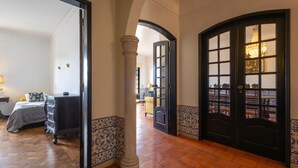 A hallway with a wooden floor, a bed with a blue and white patterned headboard, and a black door with glass panels.