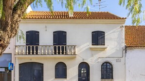 A two-story building with a balcony, large arched doors, and a tiled roof.