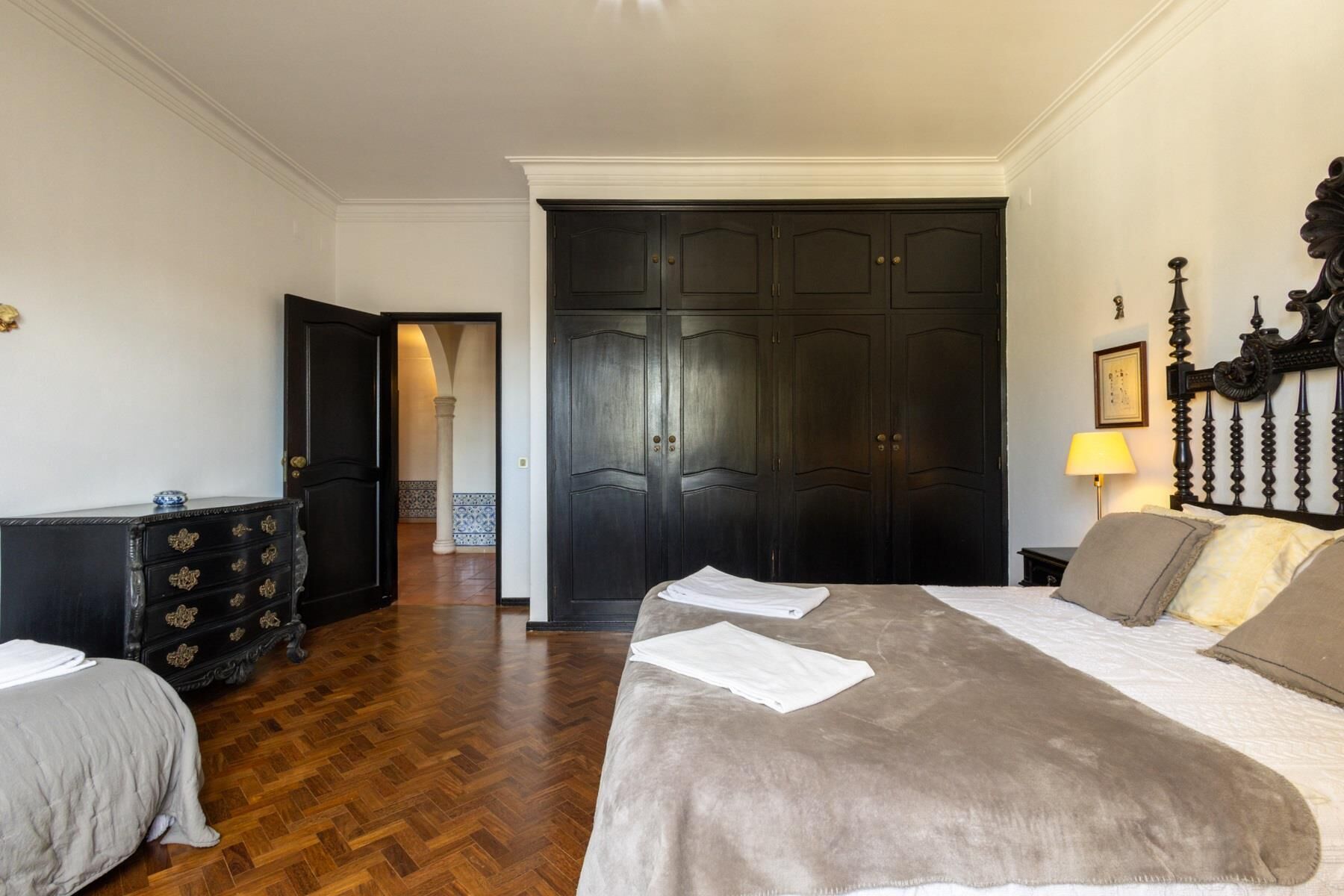 A hotel room with a large bed, a dresser, a wardrobe, and a door leading to another room.