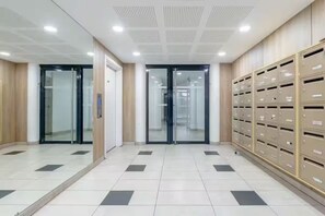 A modern elevator area with a tiled floor, glass doors, and a row of metal lockers on the right. - Head in the clouds Drancy (Near Paris, CDG) (Drancy)
