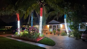 A building with a paved entrance, surrounded by palm trees and plants, with decorative lights. - Deerfield Beach Guest Studio (DEERFIELD BEACH)