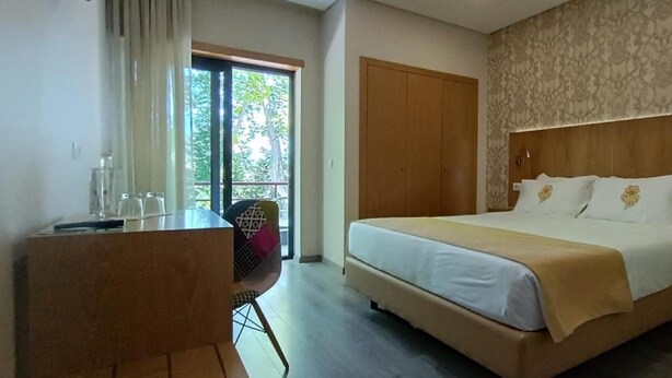 A hotel room with a bed, a desk, and a chair. There is a window with curtains, a door, and a patterned wall. - Hotel Imperio Do Minho (Ponte de Lima)
