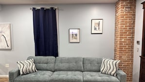A grey sectional sofa with striped pillows, a dark blue curtain, and two framed artworks on the wall. - Gray Getaway (Gettysburg)