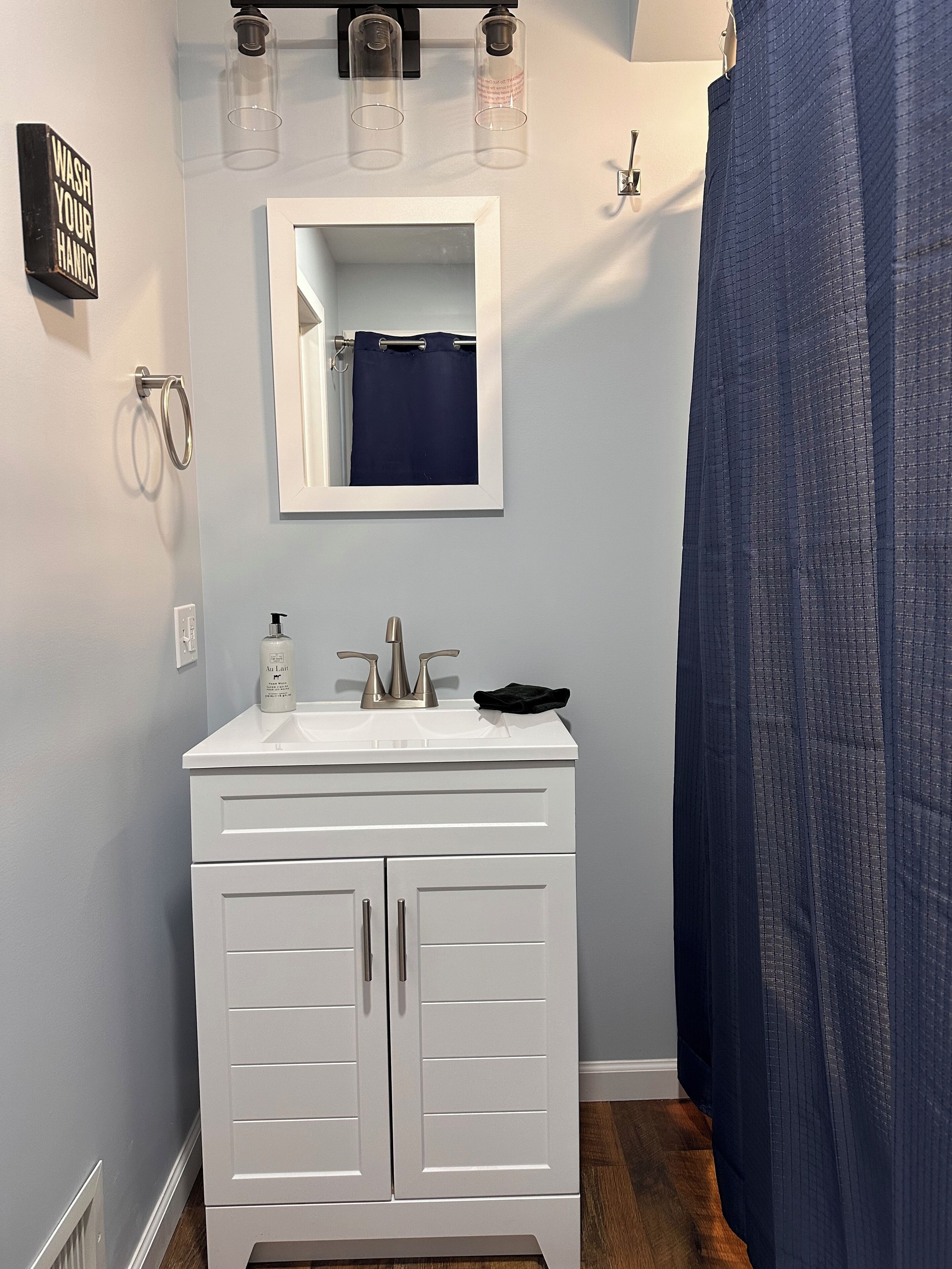 Une salle de bain avec un meuble-lavabo blanc, un miroir, un porte-serviettes et un rideau de douche.