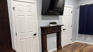 A room with wooden flooring, a fireplace, a mounted TV, and a blue curtain. - Gray Getaway (Gettysburg)