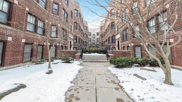 A snow-covered pathway leading to a brick building with multiple windows and a central staircase. - Beautifully Remodeled 2B/2BA Hyde Park (Chicago)