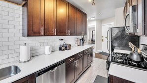 A modern kitchen with dark wooden cabinets, a white countertop, stainless steel appliances, and a black stove. - Beautifully Remodeled 2B/2BA Hyde Park (Chicago)