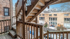 A wooden staircase leading to a balcony with a view of neighboring buildings and a brick wall. - Beautifully Remodeled 2B/2BA Hyde Park (Chicago)