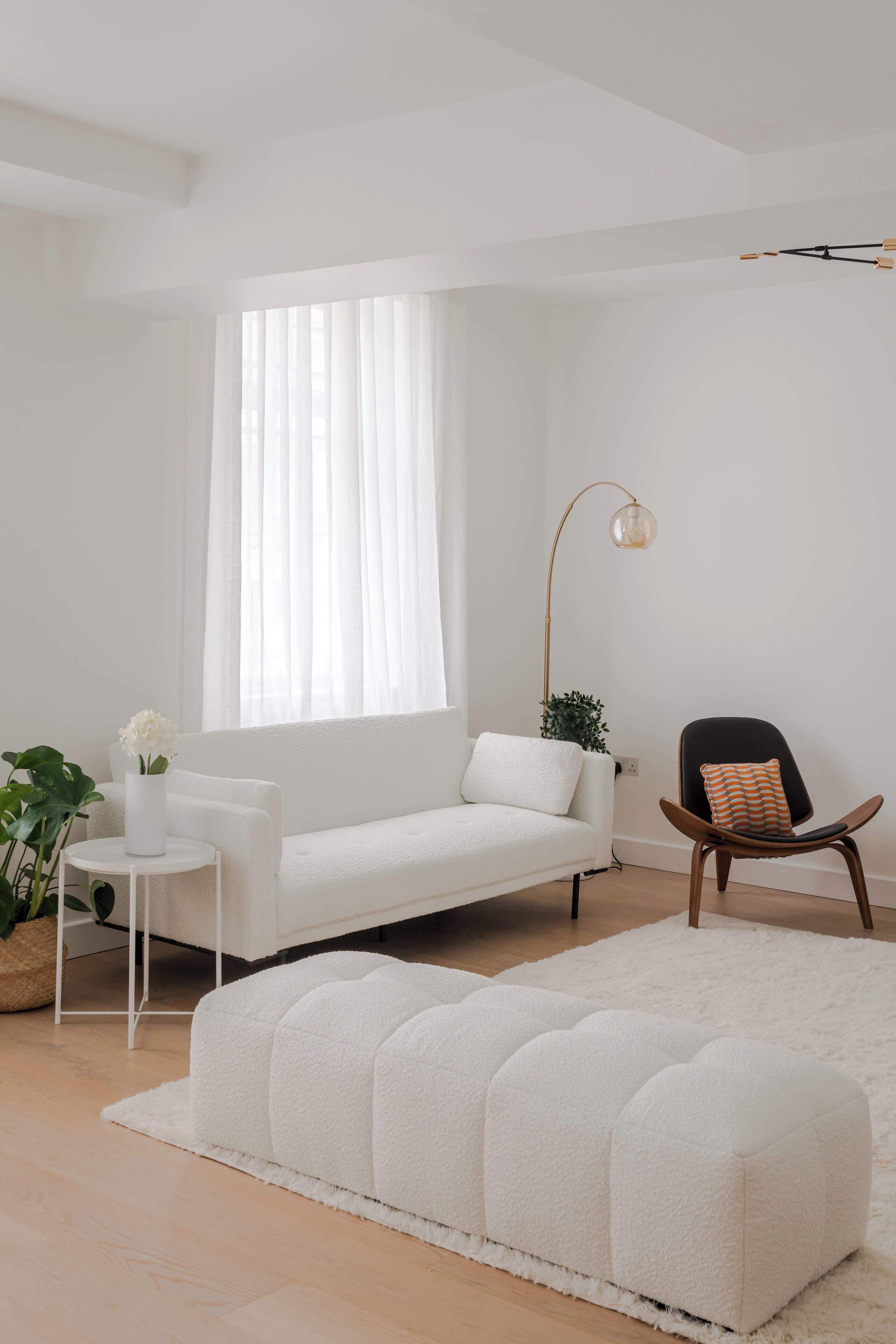 Una sala de estar moderna con un sofá blanco, una mesita redonda, una silla negra, una lámpara de pie y un reposapiés blanco.