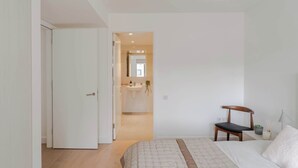Une chambre à coucher comprenant un lit, une chaise, une table de chevet avec une lampe, et donnant sur la salle de bain.