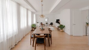 Un vaste espace de salle à manger avec une longue table en bois, entourée de chaises, dans un appartement moderne aux murs blancs et au plancher en bois.