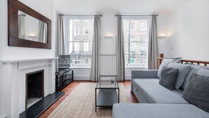 A modern living room with a fireplace, a sofa, a coffee table, and two windows with curtains. - Regency Residences - Fitzrovia - by Frankie Says (London)