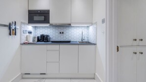 A compact kitchen with white cabinets, a built-in oven, a microwave, and a stainless steel sink. - Regency Residences - Fitzrovia - by Frankie Says (London)