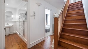 A modern hotel room with a wooden staircase, a bathroom with a white sink, and a view of the adjacent room. - Regency Residences - Fitzrovia - by Frankie Says (London)