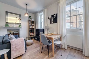 A modern living room with a sofa, a dining table with chairs, a TV, and a fireplace. - The Fox & Found - Fitzrovia - by Frankie (London)