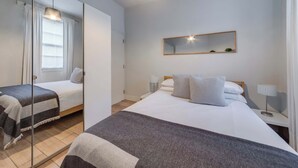 A modern hotel room with a large bed, a bedside table with a lamp, a mirror on the wall, and a window with curtains. - The Fox & Found - Fitzrovia - by Frankie (London)
