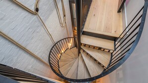 Una escalera de caracol con escalones de madera y barandillas de metal, rodeada por un muro de ladrillo blanco.