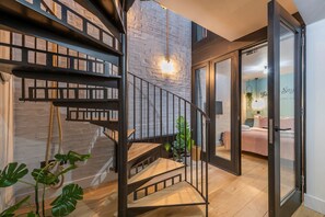 A modern interior with a spiral staircase, a visible bed in the adjacent room, and a brick wall. - The Acre Abode - Covent Garden - by Frankie (London)