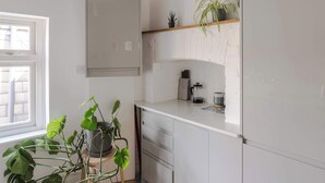 A kitchen with white cabinets, a window, and a shelf with plants. - Stairway To Heaven - Fitzrovia - by Frankie Says (London)
