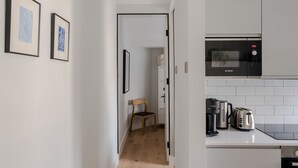 A narrow hallway leading to a kitchen with a Bosch microwave, a coffee maker, and a toaster on the counter. - Stairway To Heaven - Fitzrovia - by Frankie Says (London)