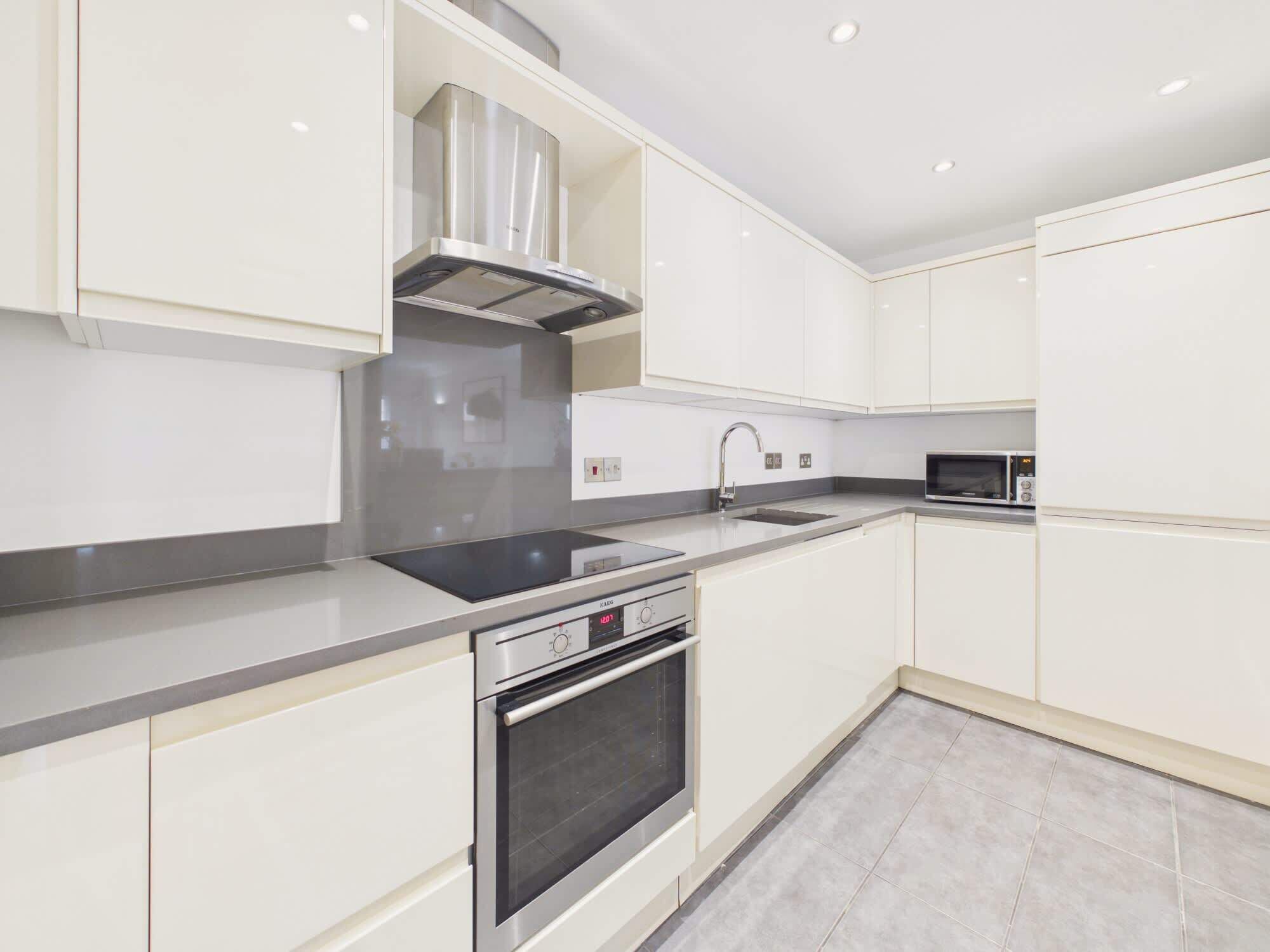 A modern kitchen with white cabinetry, a stainless steel range hood, a built-in oven, and a microwave.