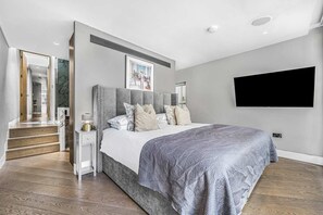 Une chambre moderne avec un grand lit, un téléviseur à écran plat et un escalier menant à une autre pièce.