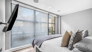 Une chambre avec une grande fenêtre, un lit avec de nombreux oreillers et un téléviseur fixé au mur.